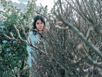 Portrait of young woman standing by tree in forest