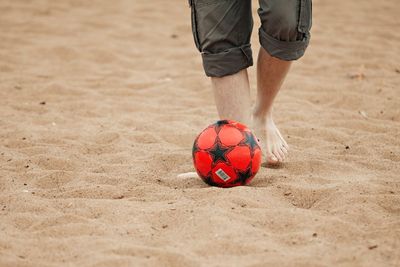 Low section of man playing soccer on sand at beach