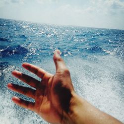 Person hand by sea against sky