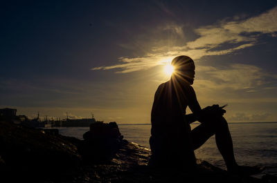 Silhouette man standing at beach against sky during sunset