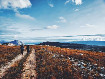 Rear view of people walking on mountain against sky