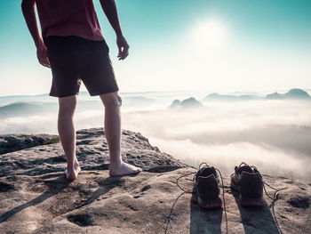 Traveler's legs, stripped light shoes and mountain peak. heavy fog and sun hanging above mist