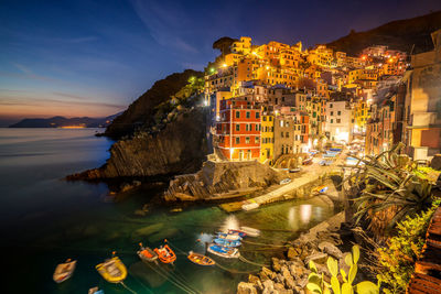 High angle view of illuminated buildings by sea against sky at night