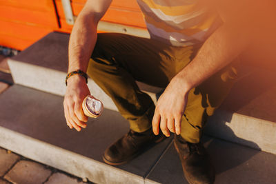 Low section of man with ice cream cone sitting on steps during sunny day