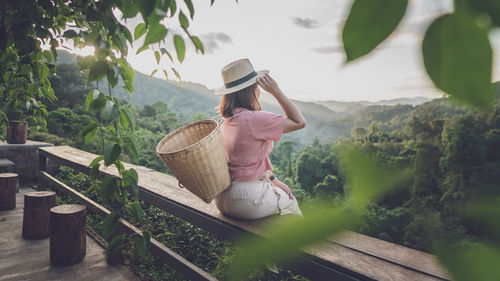 Woman carrying basket sitting on railing against sky