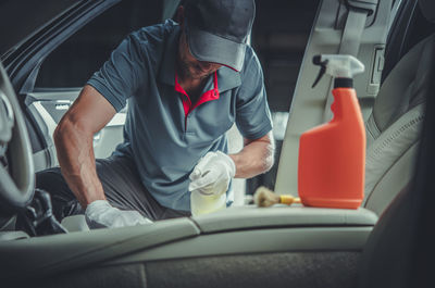 Caucasian car detailer cleaning modern vehicle interior using professional detergents. 