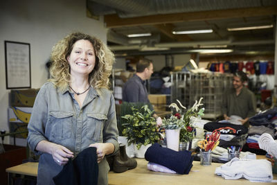 Portrait of smiling mature woman standing against colleagues working in warehouse