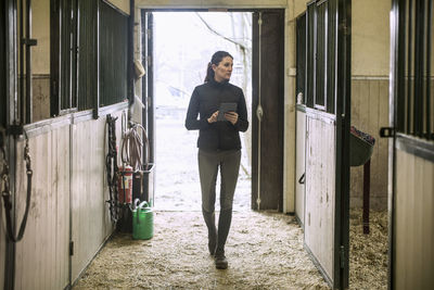 Full length of mid adult woman using digital tablet in horse stable