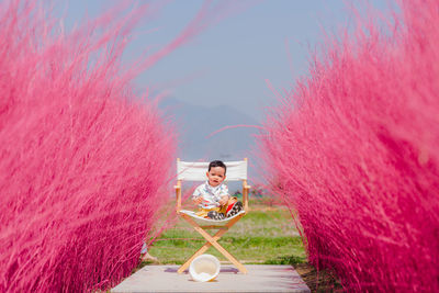 Asian child sitting on a chair in the middle of nature surrounded by pink grass