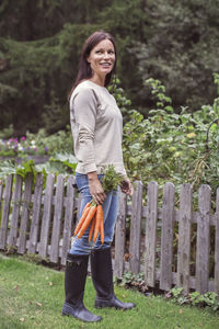 Full length of happy woman holding bunch of freshly harvested carrots at organic farm