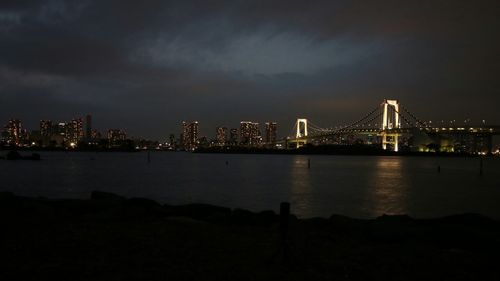 Illuminated rainbow bridge over tokyo bay against sky at night