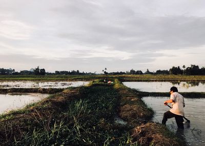 Man working at farm against cloudy sky