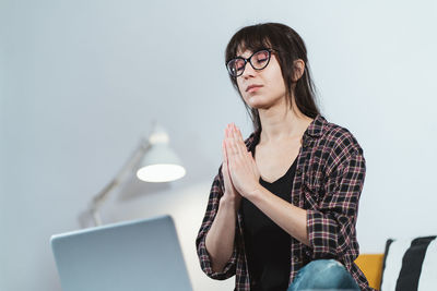 Young woman praying while sitting at home