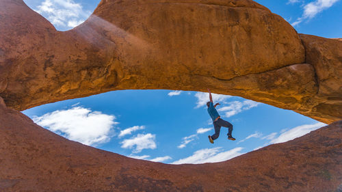 Low angle view of man climbing rock against sky
