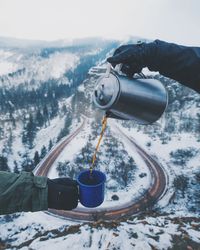 Cropped hand pouring tea for friend against mountain