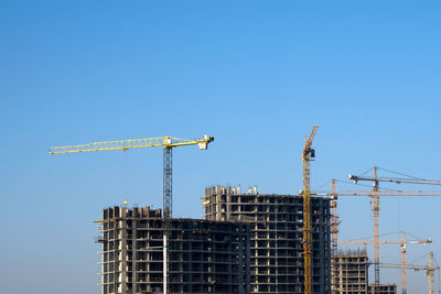 Low angle view of cranes on buildings against clear blue sky