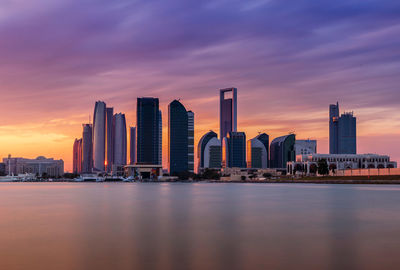 Sea by modern buildings against romantic sky at sunset
