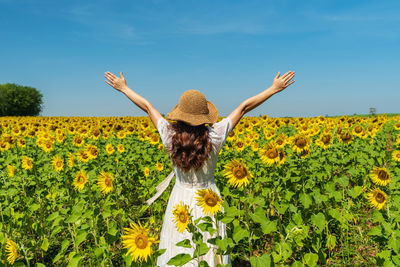Rear view of woman standing amidst yellow flowering plants on field against sky