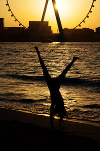 Silhouette of woman doing cartwheel at sunset