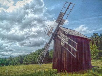 Windmills on grassy field against cloudy sky