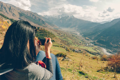 Rear view of woman photographing against mountains