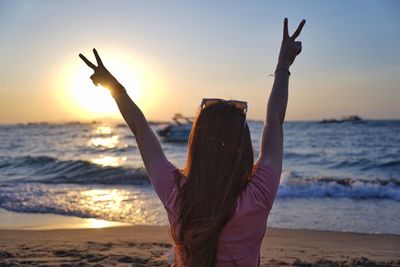 Rear view of woman standing at beach during sunset