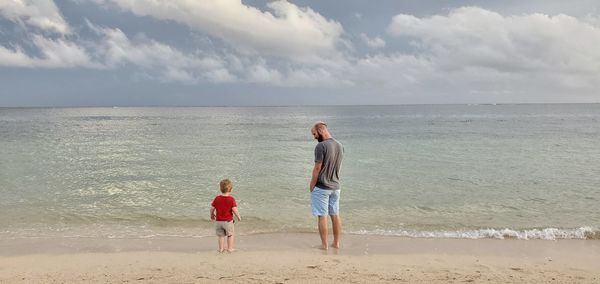 Father looking at son standing on shore at beach