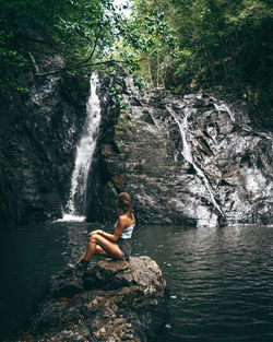 Young woman sitting on rock by waterfall