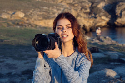 Portrait of young woman photographing on rock