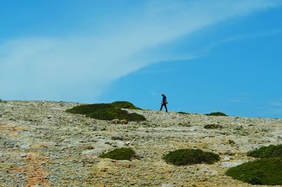 Man walking on mountain against blue sky