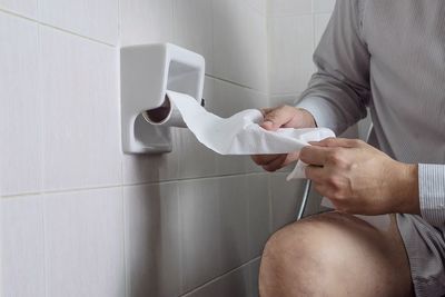 Midsection of man holding tissue paper while sitting in bathroom