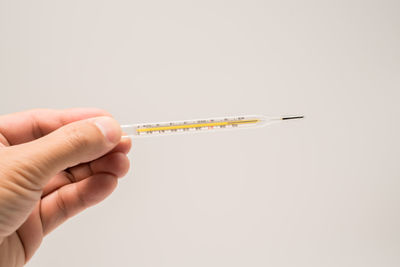 Cropped hand holding thermometer against white background