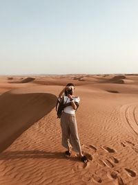 Woman photographing through camera while standing on sand dune at desert