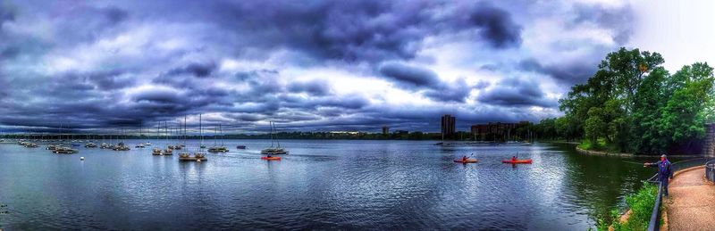 Boats in river against cloudy sky