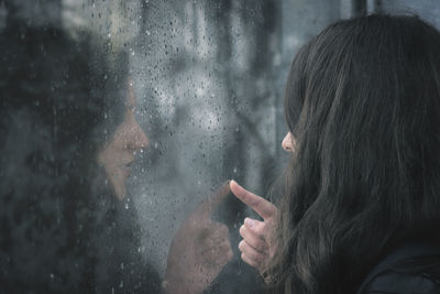 Close-up of woman looking through wet window in rainy season