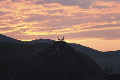 Silhouette deer on mountain against cloudy sky during sunset