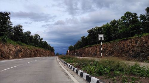 Empty road by trees against sky