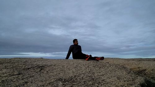 Rear view of man sitting on beach against sky