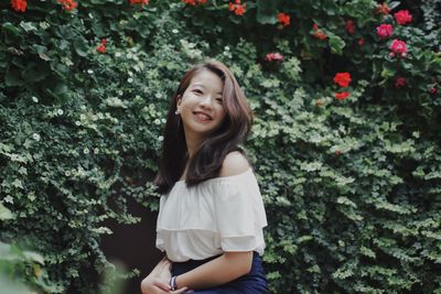 Smiling young woman standing against plants