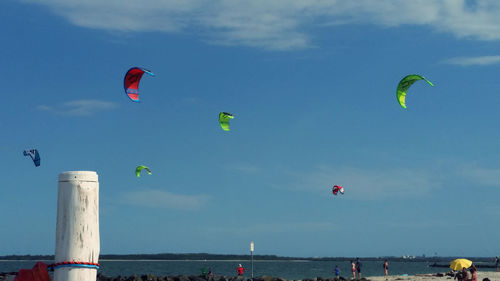 People at promenades with kites over sea against sky