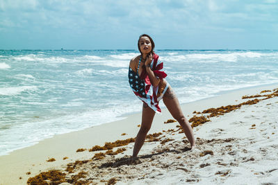 Woman with american flag at beach against sky