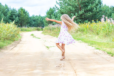 A girl with long blond curly hair is dancing, spinning on a forest road. childhood, happiness. 