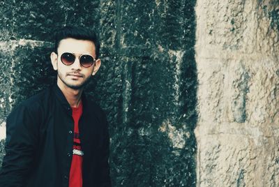 Portrait of young man wearing sunglasses standing against wall