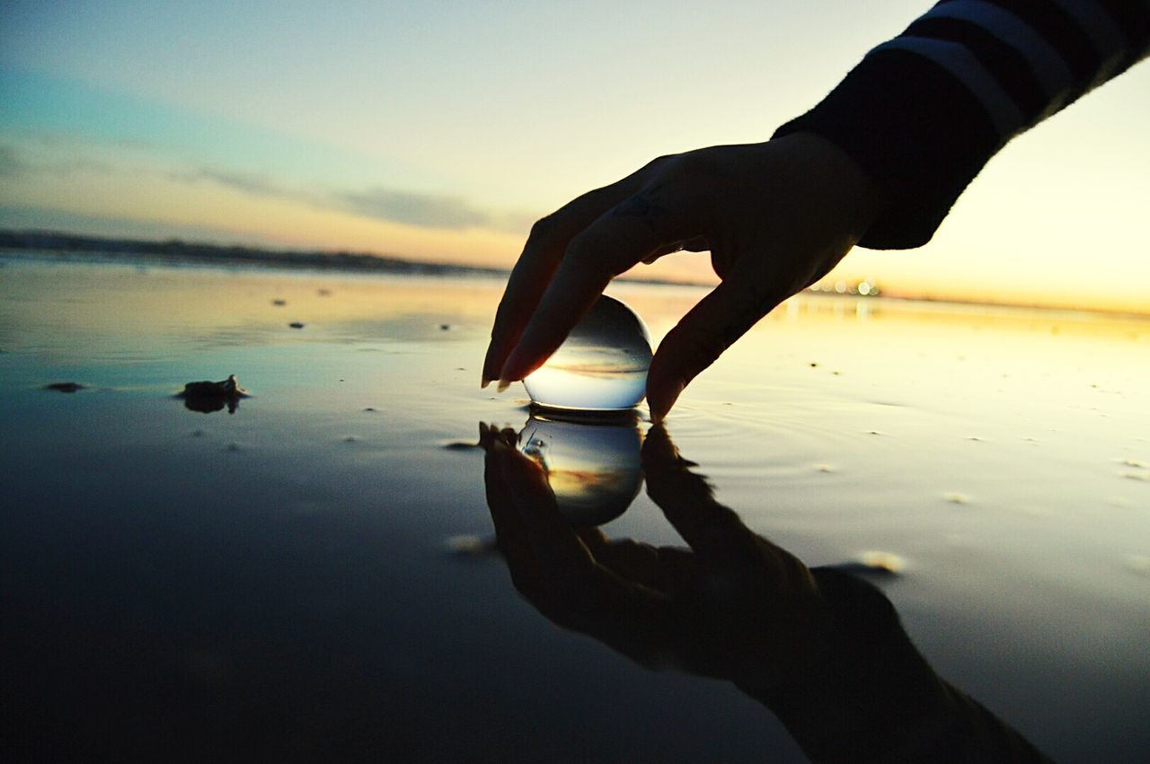 sunset, human hand, water, reflection, human finger, beach, human body part, one person, nature, beauty in nature, silhouette, real people, holding, sea, outdoors, sky, men, horizon over water, close-up, bubble wand, day, people