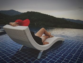 Woman sitting on lounge chair in infinity pool during sunset