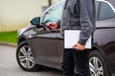 A silhouette of a man with a computer and a phone in his hands on the background of a parked car