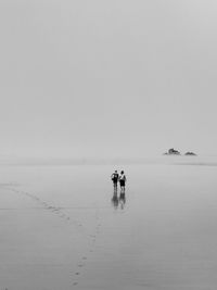 Mid distance view of man and woman walking at beach during foggy weather