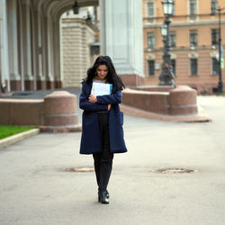 Full length of young woman with books walking outside university