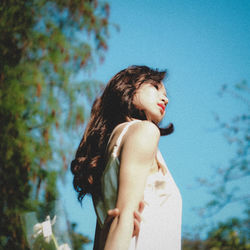 Side view of young woman standing against sky