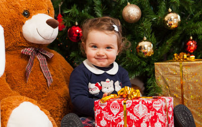 Cute girl with stuffed toy and gifts against christmas tree at home